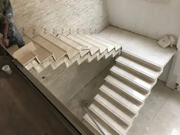 Escalera de dos tramos vista desde arriba. Tramo inferior y meseta revestidos en tono crema mientras se colocan los peldaños del tramo superior junto al aplacado en tiras.