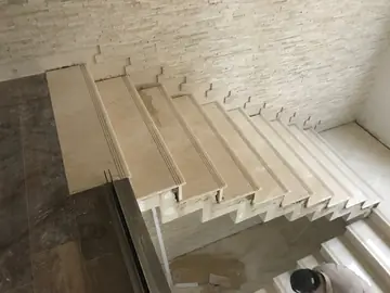 Tramo de escalera volada desde la planta alta. Peldaños en tono crema con ranuras antideslizantes que dejan ver el perfil escalonado junto a la pared de plaqueta.