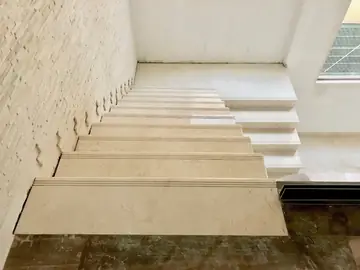 Tramo superior de la escalera revestida. Peldaños en tono crema vistos desde el desembarco, con la pared de plaqueta en tiras a un lado.