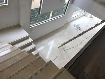 Escalera y pavimento desde la planta alta. Peldaños y pavimento en tono crema bajo el ventanal de doble altura, con la obra en fase de remates.