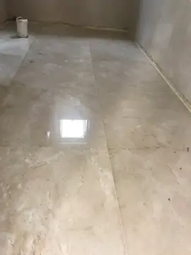 Piezas grandes pulidas en una estancia. Pavimento en tono crema con veta y reflejo de la ventana, con las paredes aún sin revestir.