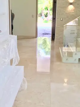 Recibidor con pavimento pulido. Pavimento en tono crema con brillo que refleja la puerta abierta, junto a una escalera con barandilla de vidrio.