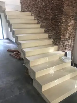 Escalera en tono claro junto a un muro oscuro. Peldaños pulidos en tono claro con el perfil escalonado a la vista, junto a una pared revestida en tiras oscuras.