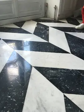 Detalle de pavimento geométrico blanco y negro. Piezas pulidas blancas y negras con veta marcada, cortadas en ángulo para formar un dibujo geométrico.