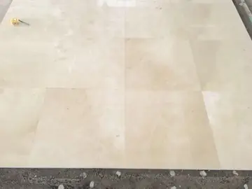 Piezas de pavimento crema recién colocadas. Detalle de piezas grandes de pavimento pulido en tono crema, recién asentadas junto al borde de la capa de mortero.