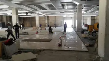 Colocación del pavimento en una nave diáfana. Cuadrilla colocando pavimento pulido en tono crema en una gran planta diáfana, con piezas acopiadas en primer plano.