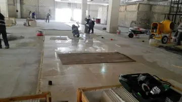 Avance del pavimento con protección de tablero. Pavimento pulido en tono crema ya colocado y protegido con un tablero mientras la cuadrilla sigue avanzando al fondo.