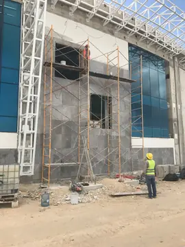 Fachada con andamio durante el aplacado. Andamio tubular frente a un paño de fachada mientras se completa el aplacado gris alrededor de los huecos.