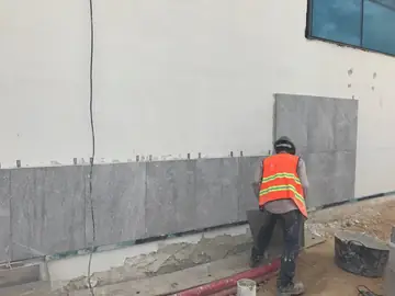 Colocación del zócalo de aplacado gris. Operario colocando piezas de aplacado gris con veta blanca en el arranque de un muro.