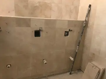 Revestimiento crema en zona de aseos. Paredes revestidas en tono crema con veta, un remate a media altura y las tomas de agua preparadas para los sanitarios.