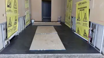 Pavimento gris oscuro protegido con tableros. Pasillo de ascensores con pavimento gris oscuro recién colocado y tableros de protección sobre las piezas.