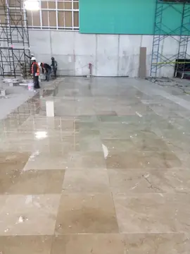 Pavimento pulido en tono beige con veta. Gran superficie de pavimento pulido en tono beige con veta, con operarios trabajando al fondo junto a los andamios.