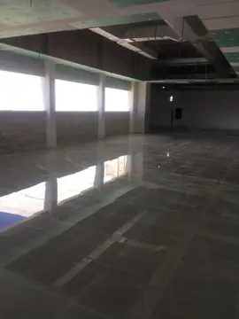 Pavimento pulido gris oscuro. Planta amplia con pavimento pulido gris oscuro en piezas grandes, con techos e instalaciones aún en obra.