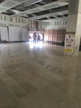 Pavimento pulido en tono beige. Gran superficie de pavimento pulido en tonos beige y gris; al fondo continúan los trabajos de techos.