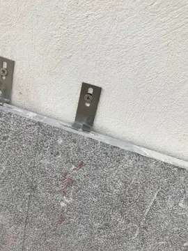 Grapa de anclaje sobre aplacado gris. Detalle de una grapa metálica de anclaje sobre el canto de una pieza gris de grano fino.