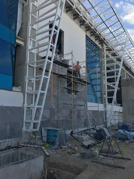 Aplacado de fachada con andamio. Fachada durante la colocación del aplacado gris con vetas blancas, con andamio tubular y estructura metálica blanca por delante.