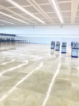 Zona de facturación con suelo en tono crema. Pavimento pulido en tono crema con vetas suaves en una sala diáfana con quioscos de autofacturación y mostradores al fondo.