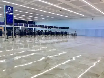 Sala de facturación con suelo pulido. Pavimento pulido en tono crema con vetas marcadas ante una fila de mostradores de facturación y un tótem de señalización.