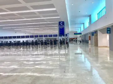 Vestíbulo de facturación con luz natural. Pavimento pulido en tono crema a lo largo del vestíbulo, con filas de mostradores a la izquierda y ventanales altos a la derecha.