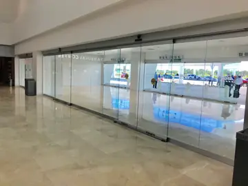 Frente acristalado con pavimento pulido. Pavimento en tono crema con vetas junto a un frente de puertas automáticas de vidrio que dan al exterior.
