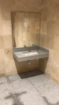 Lavabo en hornacina revestida. Hornacina con paredes revestidas en tono crema, encimera gris moteada con lavabo bajo espejo y suelo gris a juego.