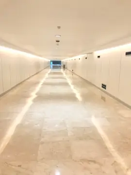 Pasillo con pavimento en tono crema. Pasillo largo con pavimento pulido en tono crema, paredes blancas de paneles y luz indirecta en el techo.