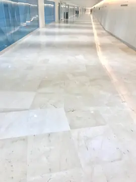 Piezas de pavimento claro en un corredor. Vista cercana del pavimento pulido en tono crema claro con vetas finas a lo largo de un corredor acristalado.
