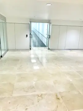 Acceso a rampa con suelo en tono crema. Pavimento pulido en tono crema con vetas ante unas puertas de vidrio que dan paso a una rampa.