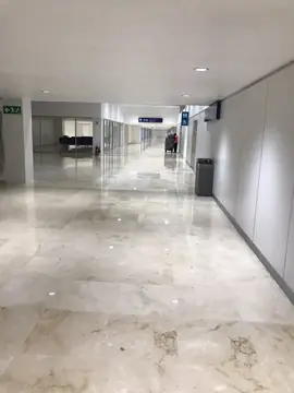 Pasillo de conexión con suelo pulido. Pasillo amplio con pavimento pulido en tono crema con vetas marcadas y paredes blancas de paneles.