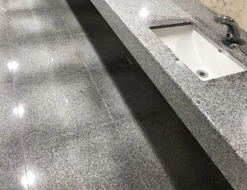 Encimera gris moteada con lavabo bajo encimera. Detalle de encimera gris moteada con lavabo bajo encimera, sobre pavimento pulido gris a juego.