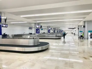 Sala de recogida de equipajes. Sala de cintas de equipaje con pavimento pulido en tono crema en piezas grandes y columnas grises numeradas.