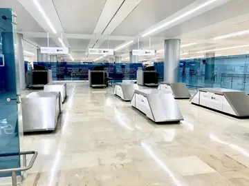 Zona de control con pavimento pulido. Pavimento pulido en tono crema con vetas en una zona de revisión con mesas de acero y escáneres al fondo.