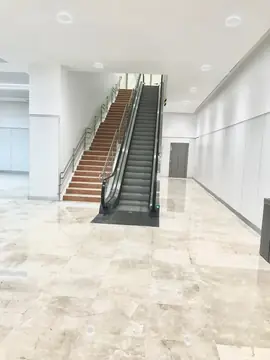 Escalera y mecánica en paralelo. Escalera de peldaños en tono rojizo junto a una escalera mecánica, con pavimento pulido en tono crema a pie de escalera.