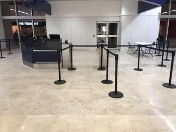 Mostrador de embarque sobre pavimento pulido. Pavimento pulido en tono gris claro con vetas y banda en tono crema delante de un mostrador de embarque con postes separadores.