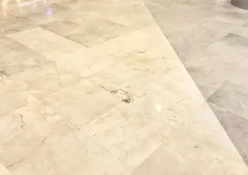 Encuentro diagonal de pavimento crema y gris. Pavimento pulido en tono crema con vetas que se encuentra en diagonal con piezas en tono gris claro.
