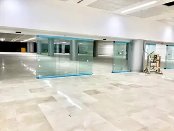 Pavimento terminado junto a mamparas. Pavimento pulido en tono crema ya colocado en una sala todavía en obra, con mamparas de vidrio aún con protecciones.