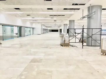 Pavimento terminado con techo en montaje. Gran sala con el pavimento pulido en tono crema ya terminado, andamios y mobiliario embalado mientras se completa el techo.