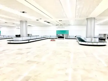 Sala de equipajes en fase de remates. Pavimento pulido en tono crema terminado alrededor de las cintas de equipaje, con el falso techo aún abierto.