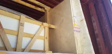 Tablero en tono crema cargado en contenedor. Tablero en tono crema con vetas suaves, colocado en vertical junto a una caja de madera dentro del contenedor.