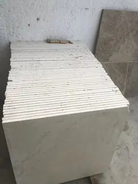 Pila de baldosas en tono crema claro. Pila de baldosas en tono crema claro con los cantos a la vista, apoyada junto a una pieza gris.