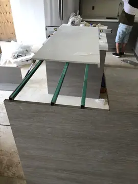 Montaje de isla y barra de cocina. Perfiles metálicos sobre el mueble de la barra y, detrás, encimera blanca aún con restos de film protector.