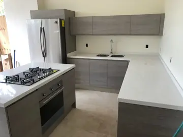 Vista de la cocina con isla y horno. Cocina con encimeras blancas en U y en la isla con placa de gas y horno integrado.
