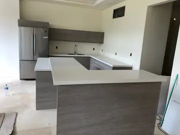 Península en L con encimera blanca. Península con encimera blanca en L delante de la cocina, con frentes grises de veta tipo madera.