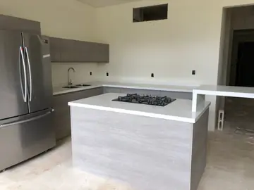 Isla y barra con encimera blanca. Cocina en obra: isla con placa de gas y barra con lateral vertical en blanco, junto al frigorífico y el tramo del fregadero.