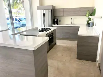 Cocina en U con barra y pavimento crema. Barra con encimera blanca, isla con placa y horno y cocina en U, sobre pavimento pulido en tono crema.