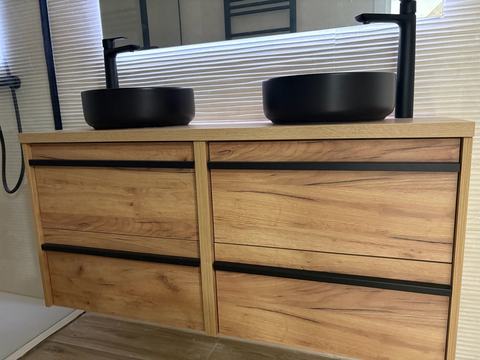 Mueble de doble lavabo. Mueble suspendido de cuatro cajones en acabado roble, con tiradores negros, dos lavabos negros sobre encimera y grifería alta negra.