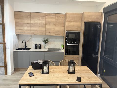 Cocina abierta al comedor. Columna de horno, frigorífico negro y encimera de mármol abiertos a la mesa.