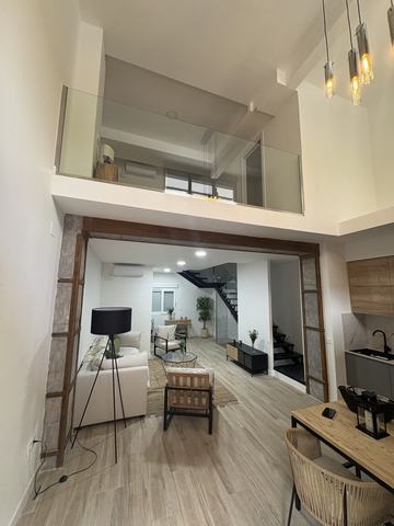 Comedor y cocina a doble altura. La doble altura queda sobre el comedor y la cocina, con altillo abierto y barandilla de vidrio. Al fondo, pasado el pórtico de hierro original, el salón con techo a altura normal y la escalera metálica negra.