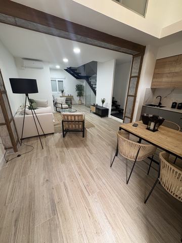 Salón, comedor y cocina abierta. La viga vista y las dos pilastras forradas de piedra enmarcan el paso al salón. A este lado quedan el comedor y la cocina abierta, con porcelánico efecto madera en toda la zona.