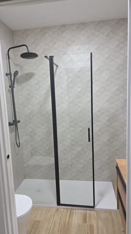 Ducha con mampara negra. Plato extraplano blanco con sumidero cuadrado, mampara de perfil negro con hoja practicable y columna de ducha negra con rociador redondo, sobre alicatado en relieve.
